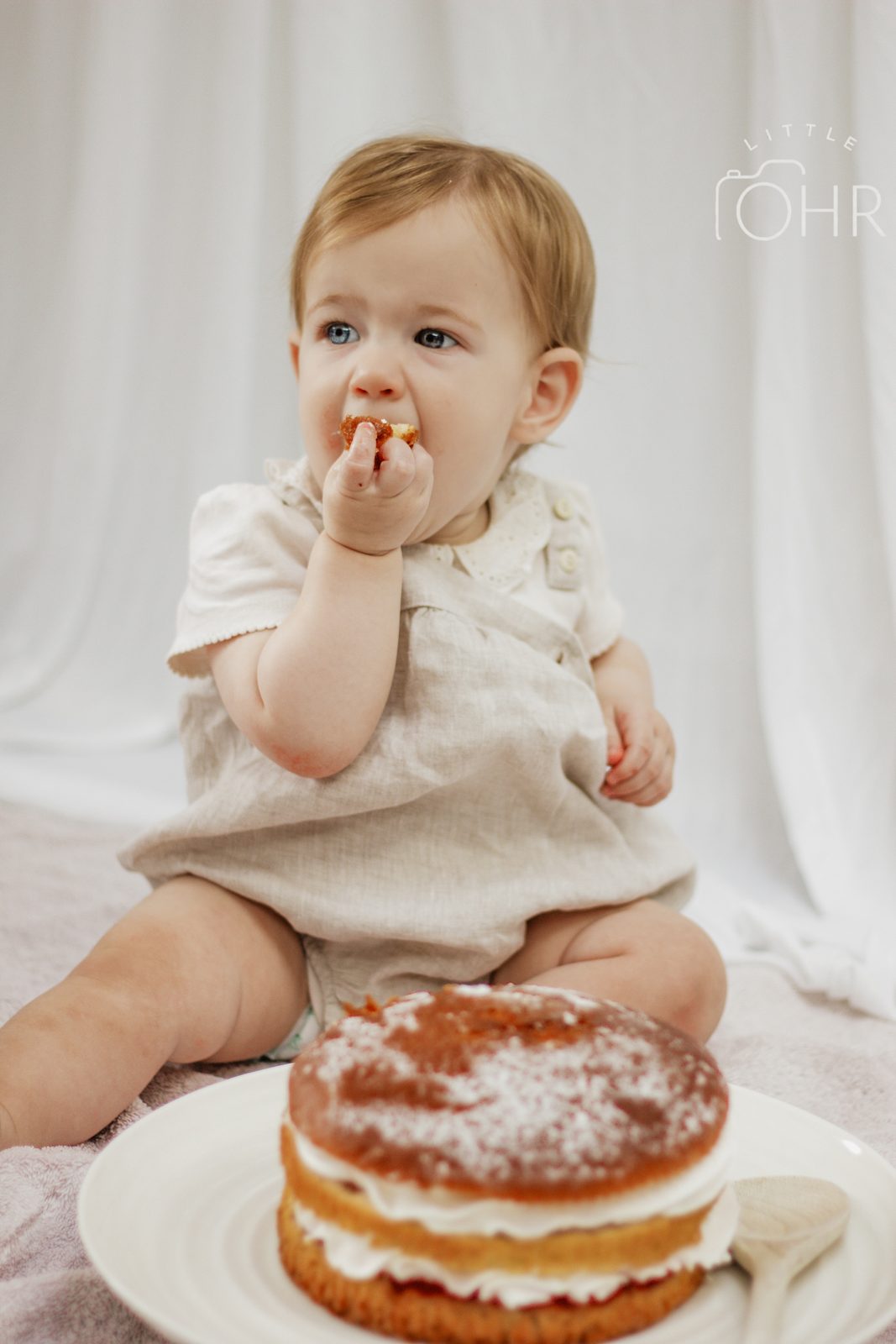 Baby tasting cream from their fingers with the cake in front of them