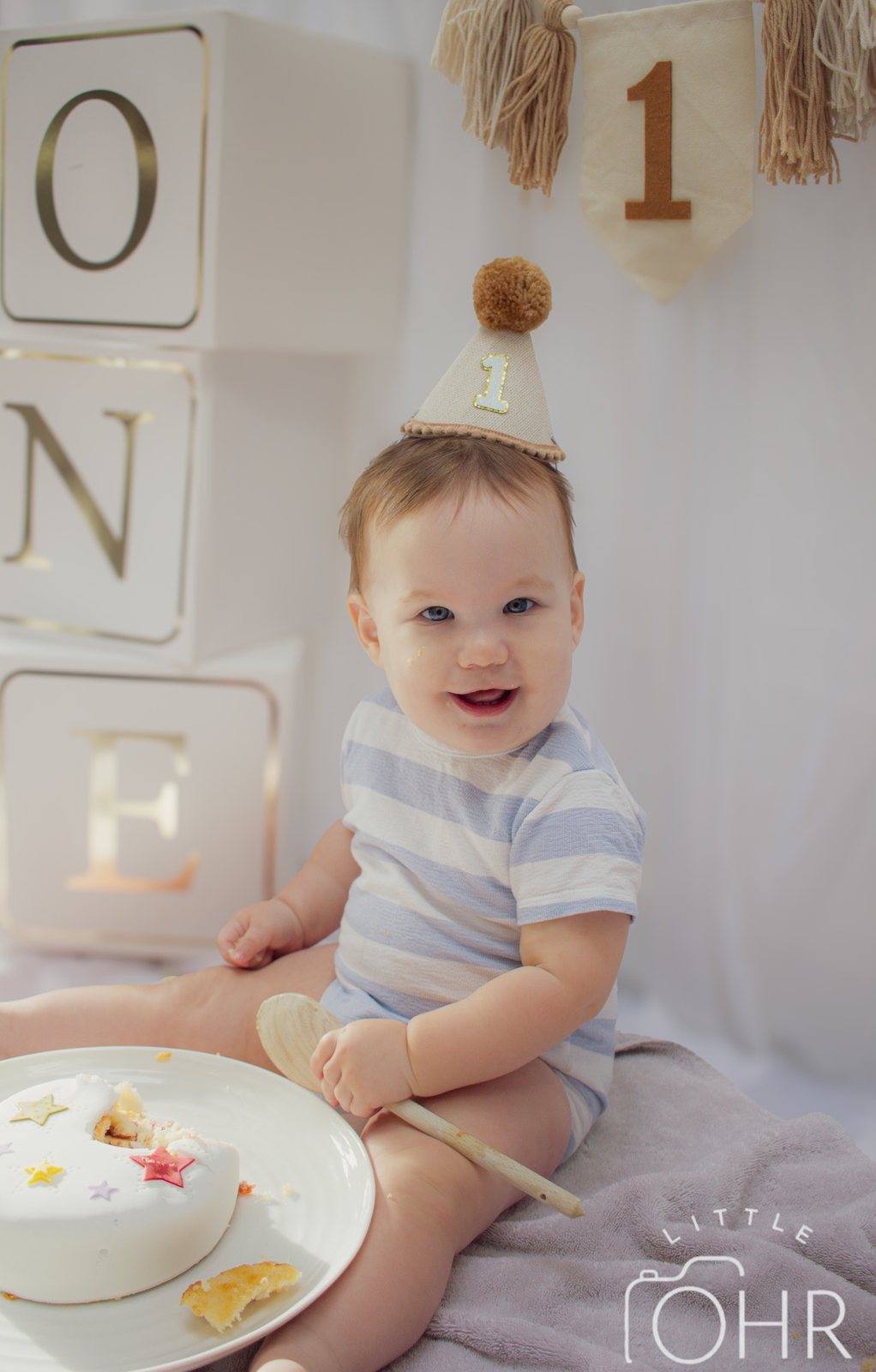 Laughing baby in a party hat next to ONE letter blocks and his cake