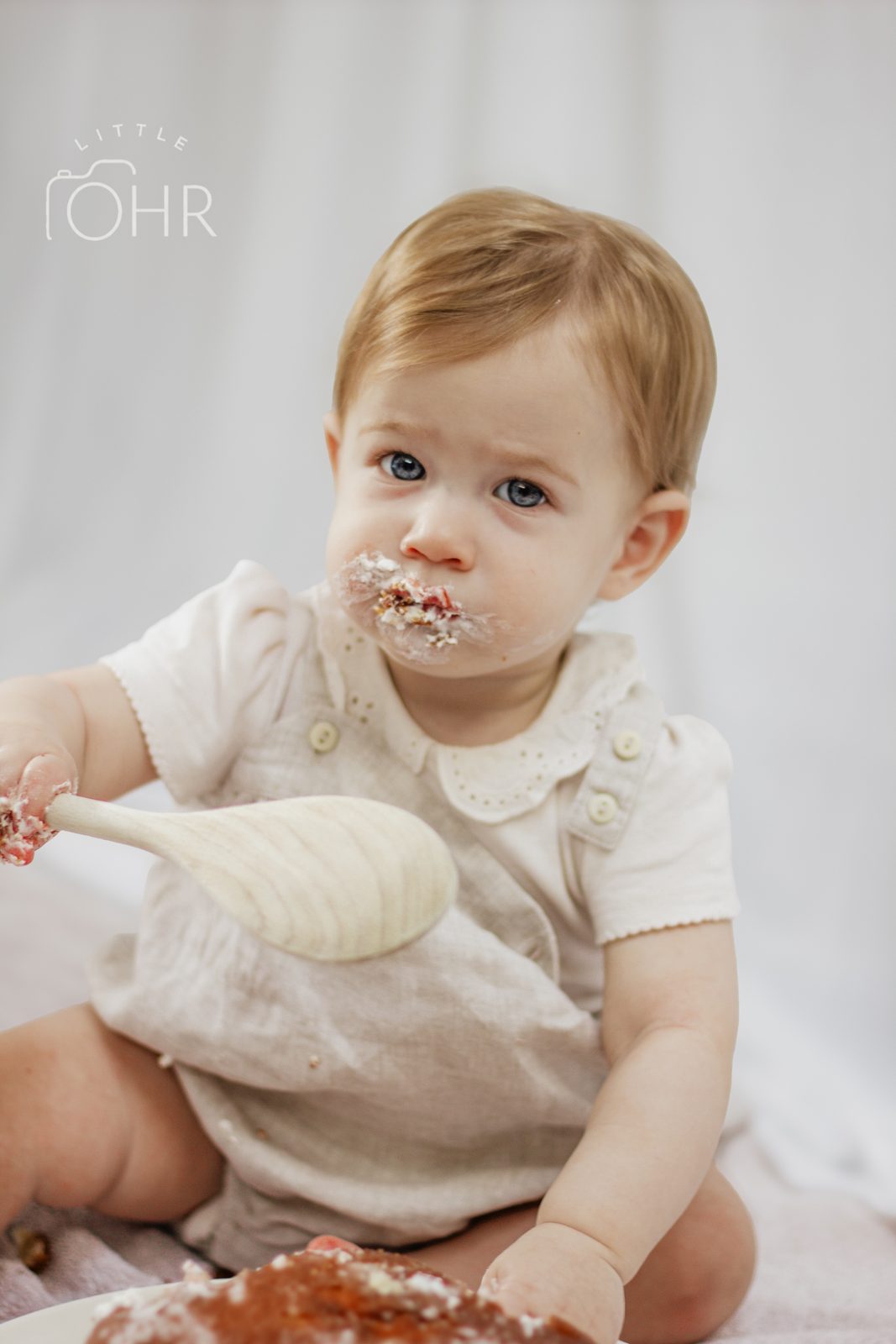 Baby with a mouthful of cake holding a wooden spoon