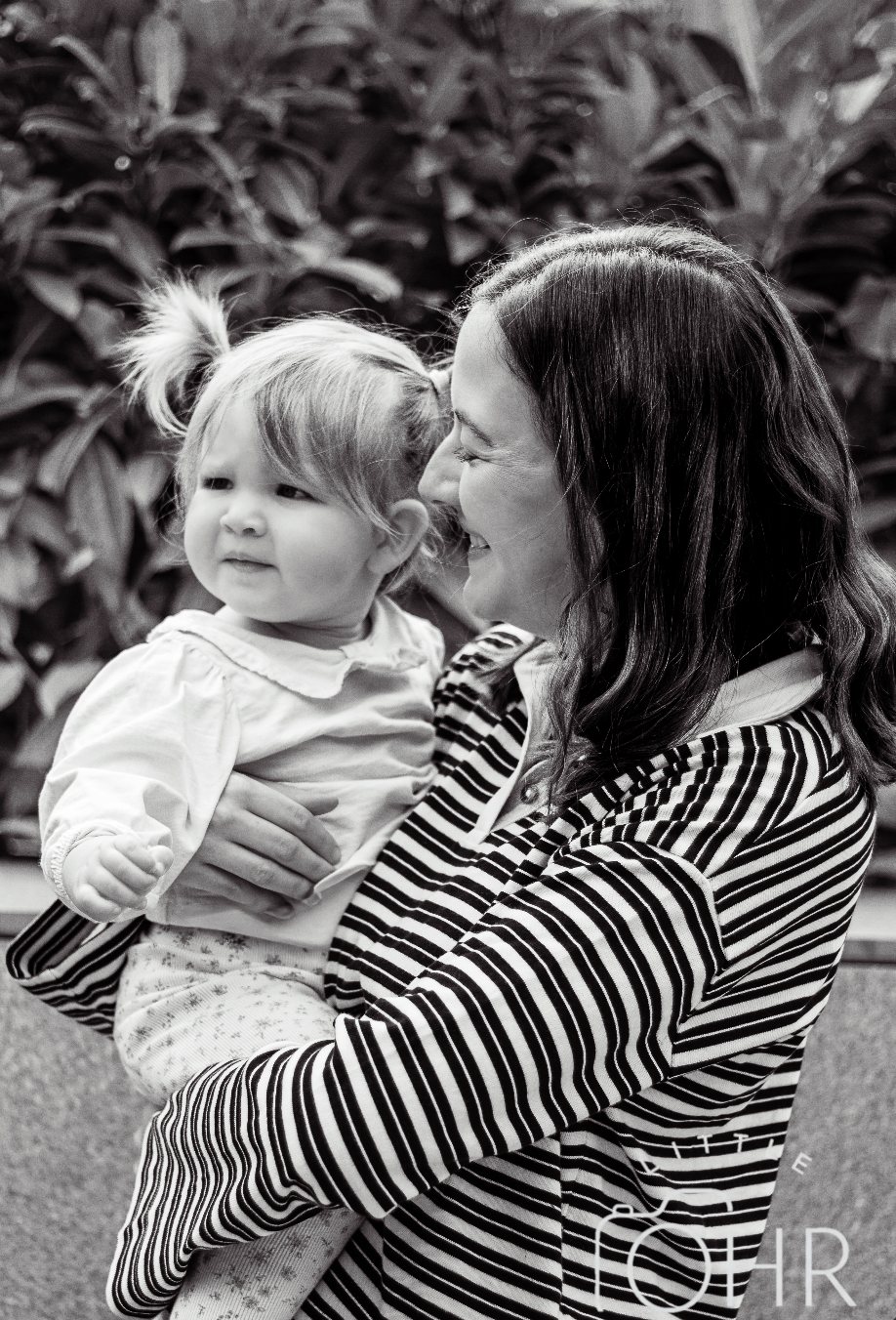 Black and white photo of mum kissing her little girl outdoors