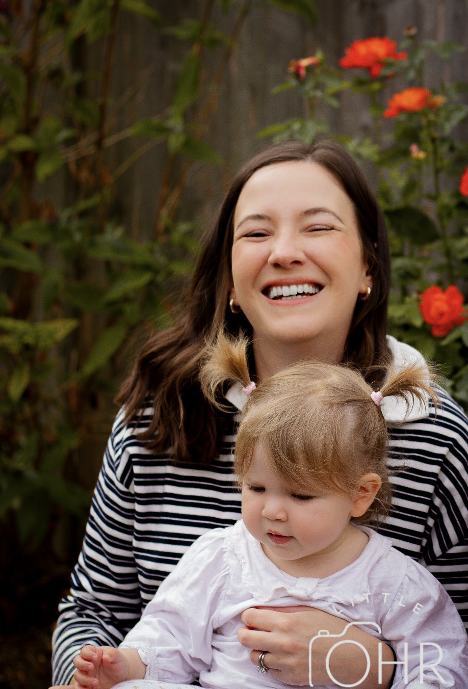 Mum laughing with her little girl in front of red roses