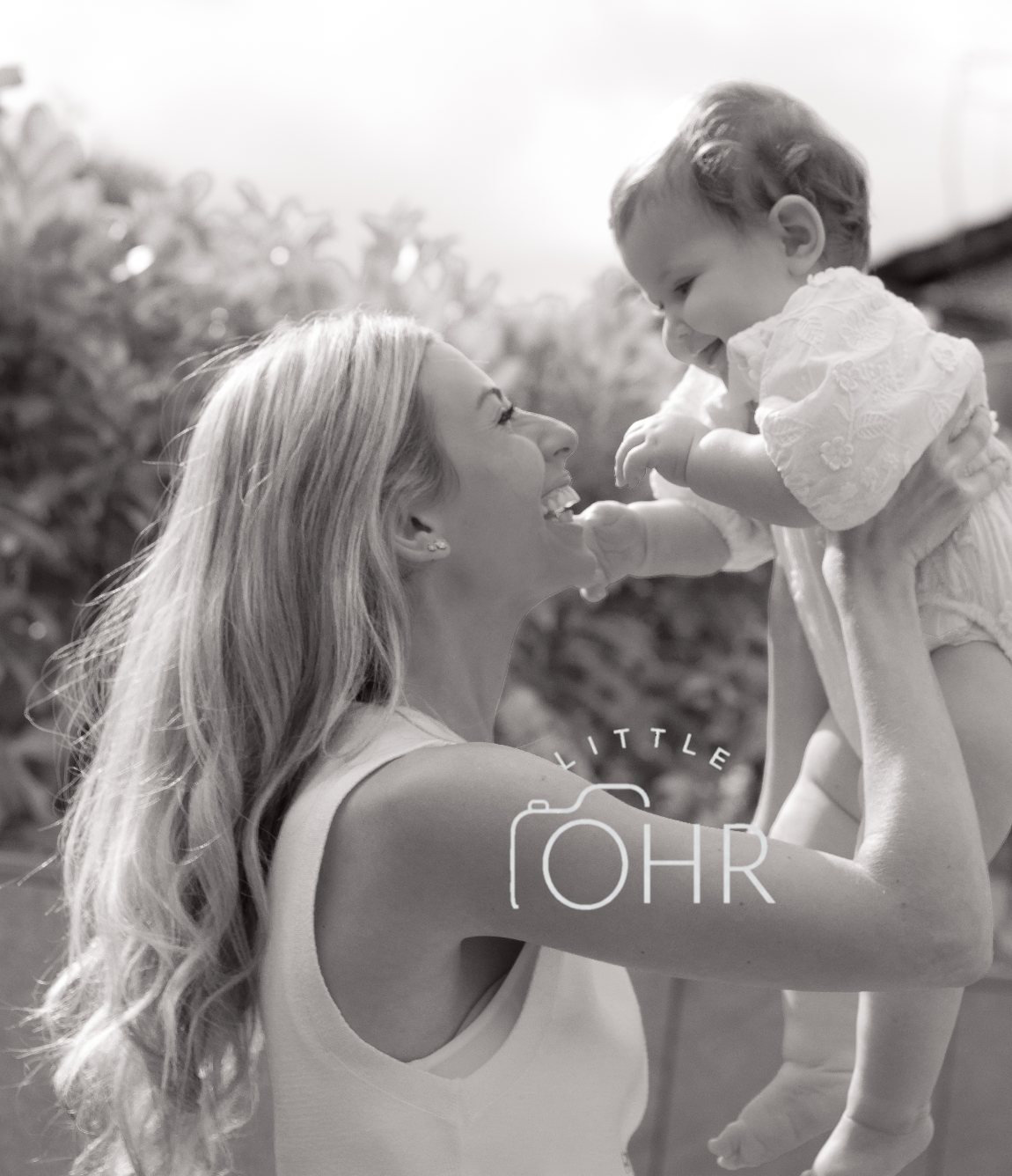 Black and white photo of a mum lifting her laughing baby in the air