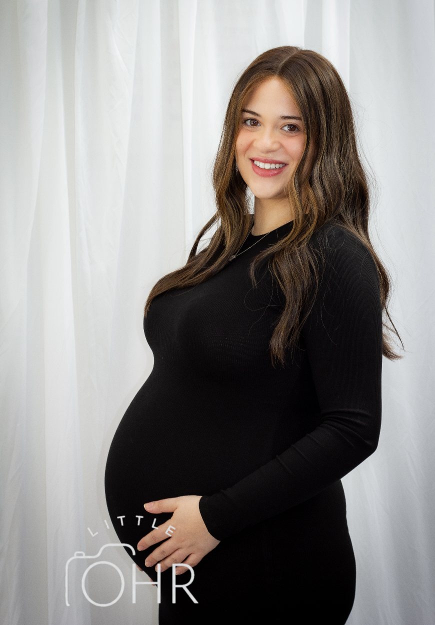 Expectant mum in a black dress cradling her bump in the studio