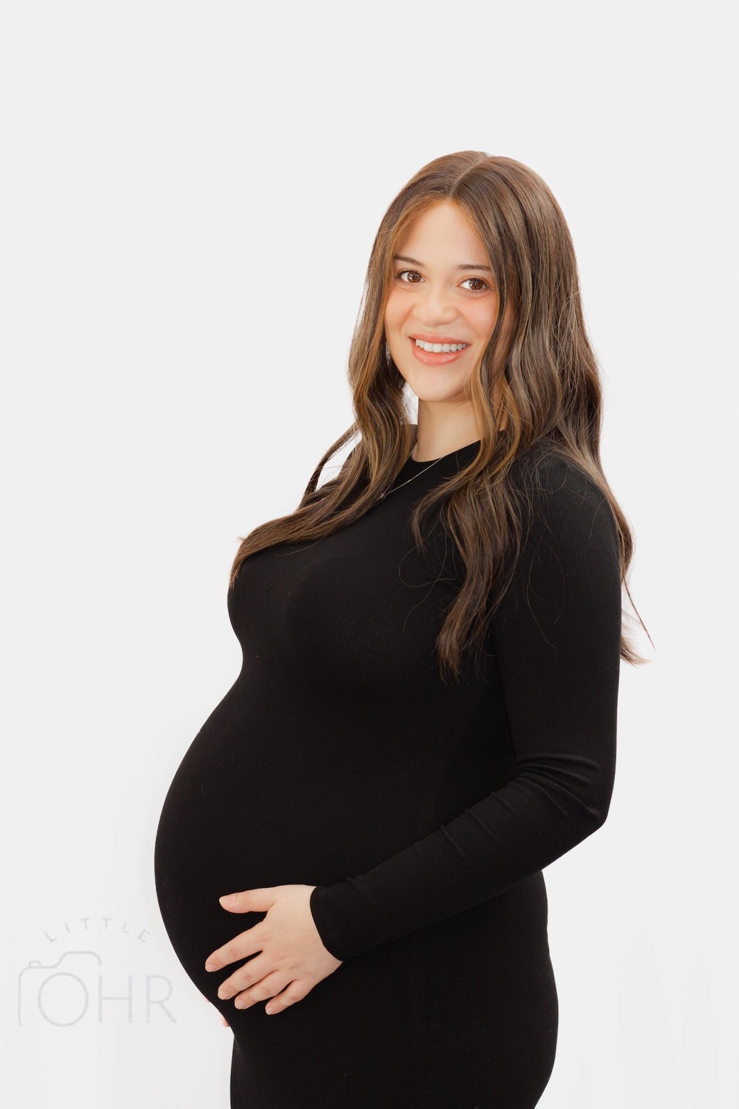 Expectant mum in a black dress smiling, hands cradling her bump, on a white background