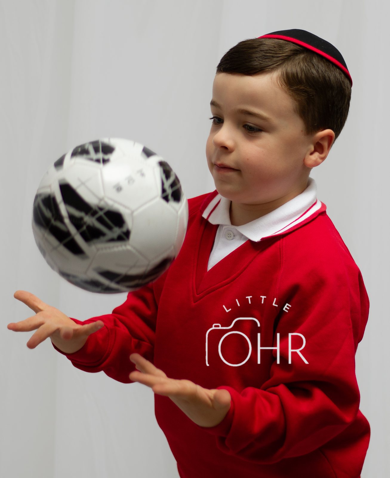 Boy in a red school jumper catching a football