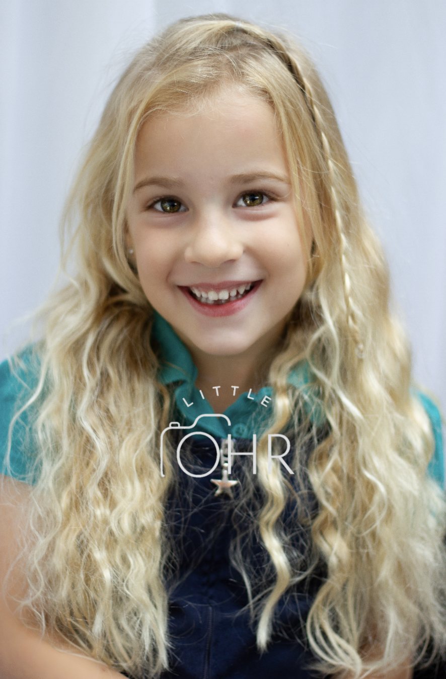Smiling girl with long wavy blonde hair in a teal school polo shirt