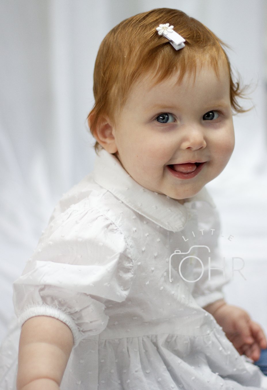 Baby girl in a white dress with a flower hair clip, laughing