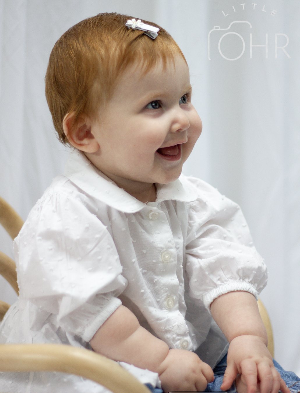 Baby girl in a white blouse laughing as she looks to the side
