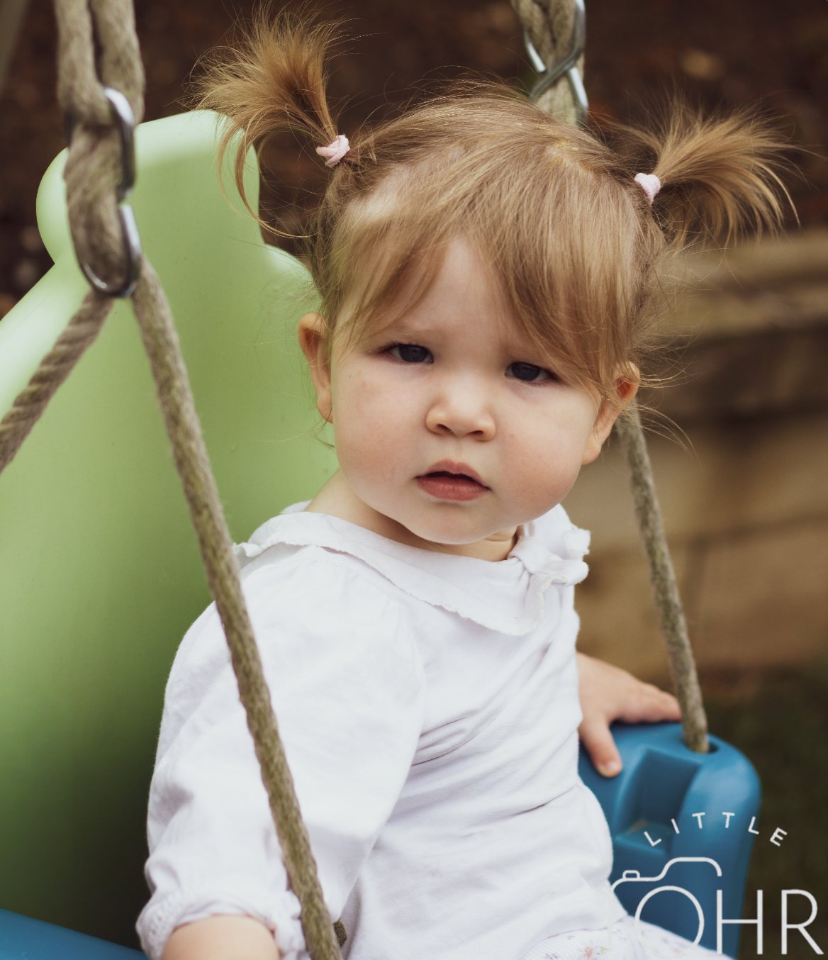 Baby girl in a white blouse sitting in a garden swing