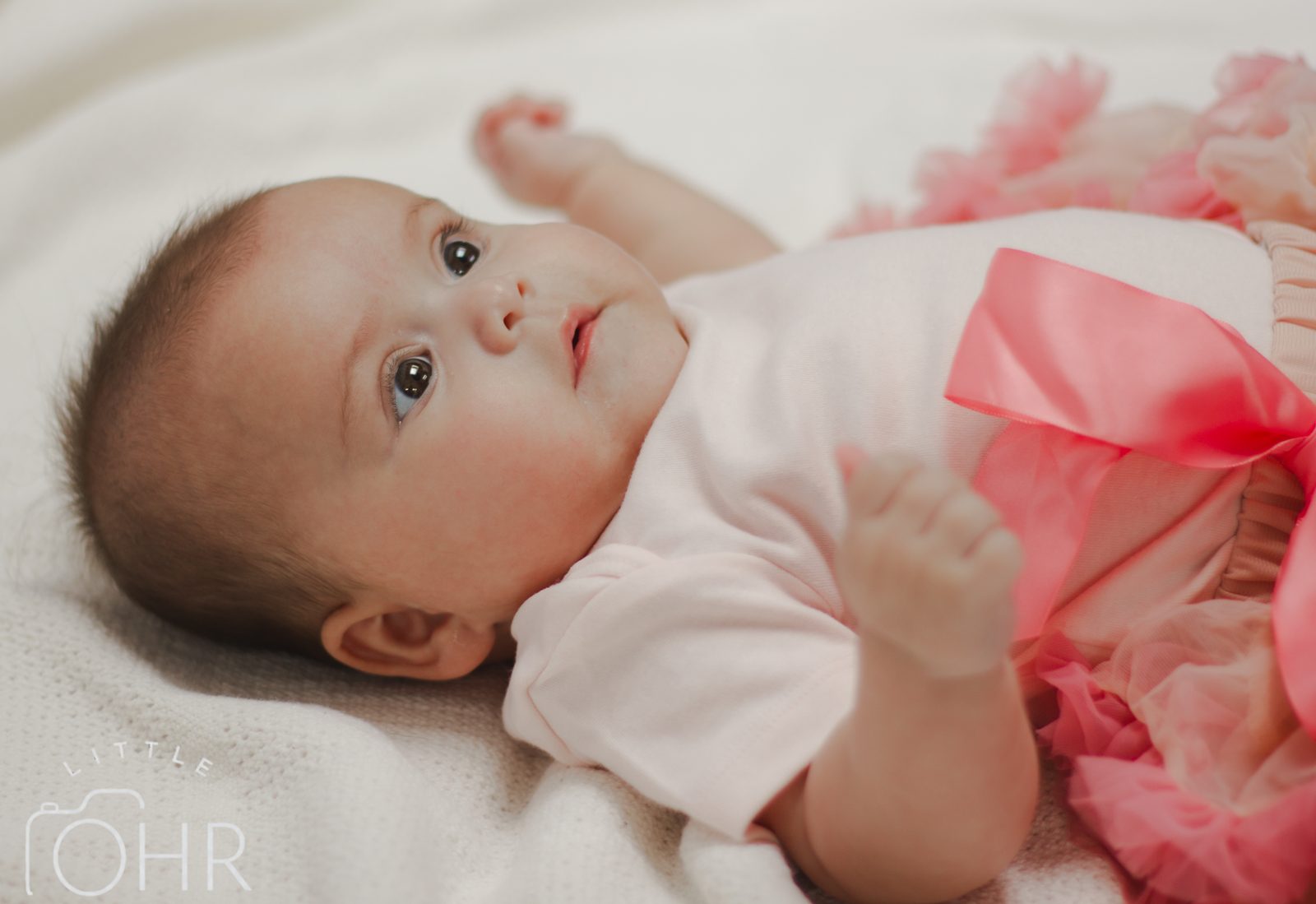 Baby girl in a pink tutu lying on a soft blanket, looking up