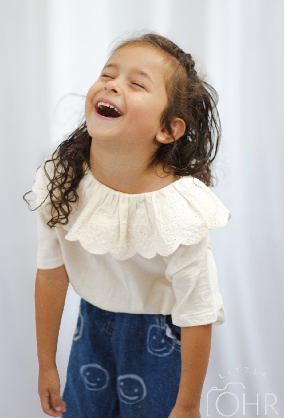 Young girl in a cream frilled collar top laughing with her head back
