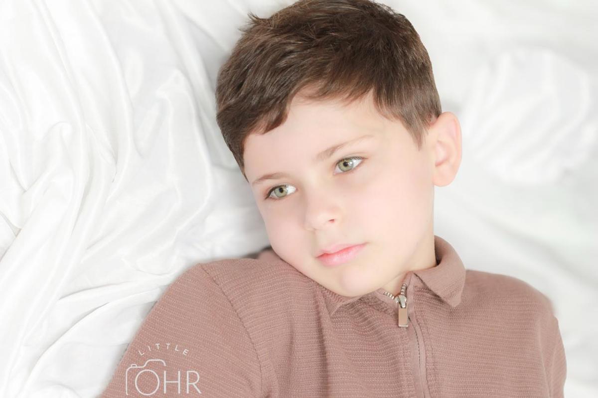 Boy in a brown polo shirt lying on a white blanket