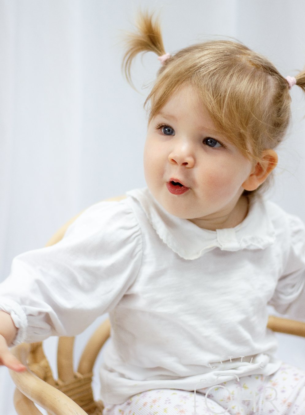 Toddler girl in a white blouse mid chatter against a soft backdrop