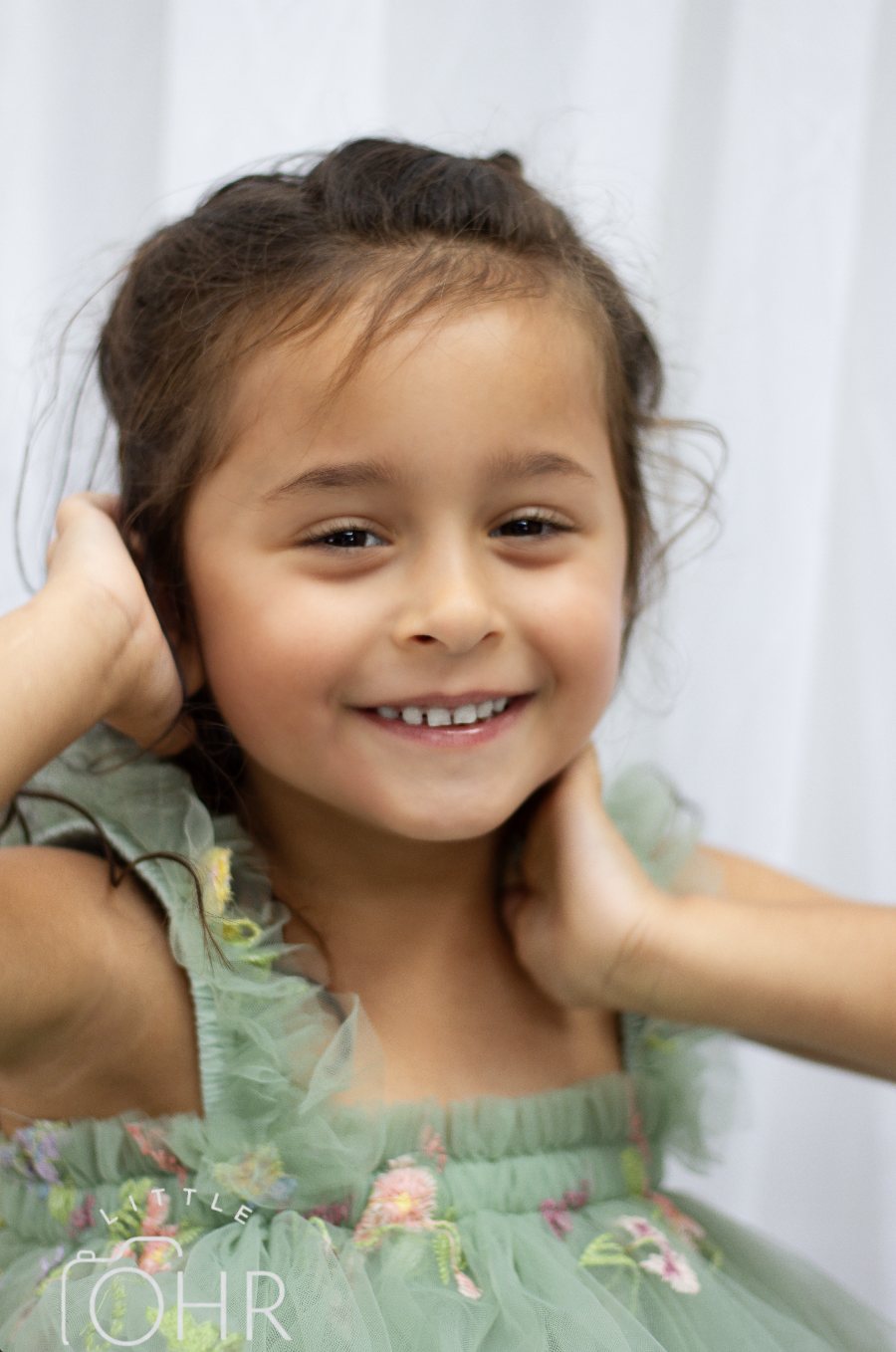 Young girl in a green tulle dress with her hands in her hair, smiling