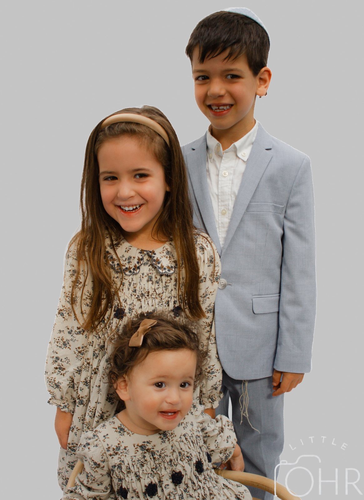 Brother in a pale blue suit standing beside his two sisters in matching floral dresses
