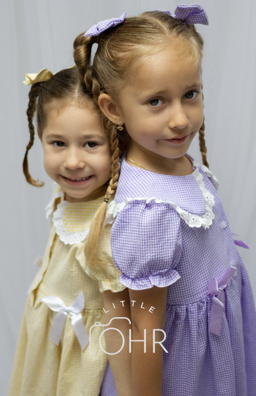 Two sisters back to back in yellow and lilac gingham dresses