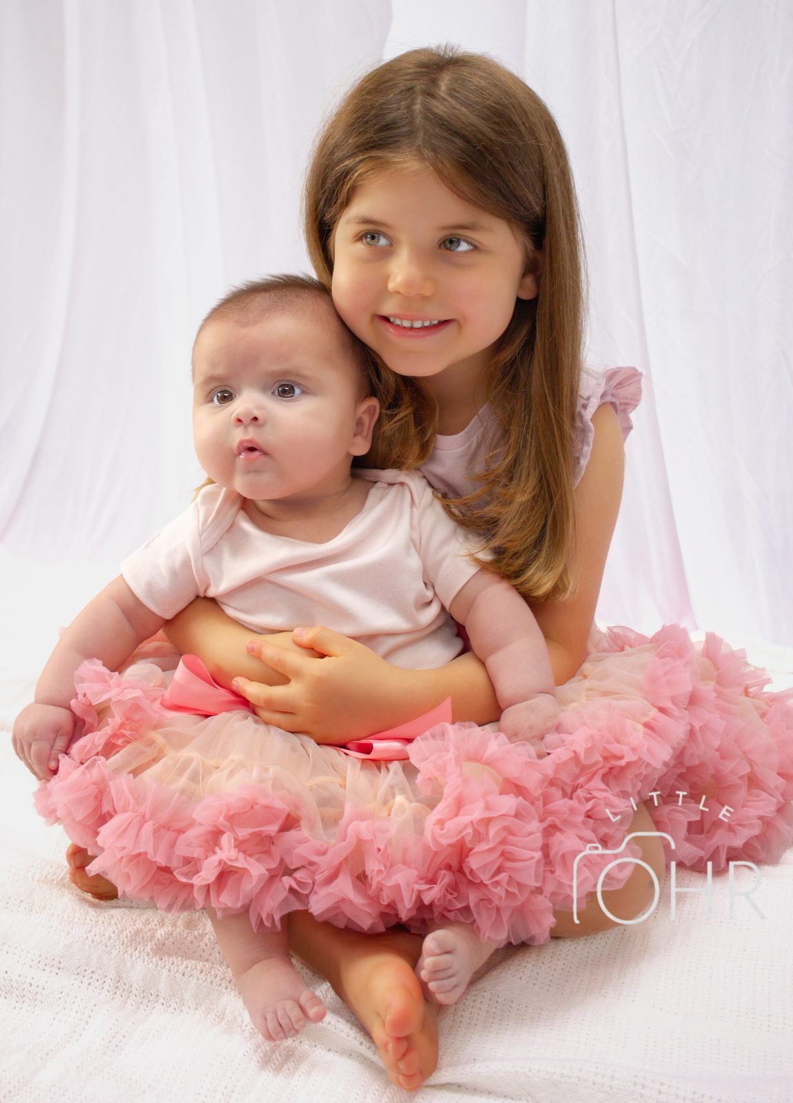 Big sister in a pink tutu holding her baby sister on her lap