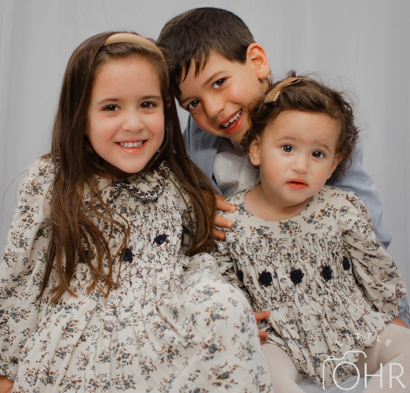 Big sister, big brother and baby sister cuddled together, the girls in matching floral dresses